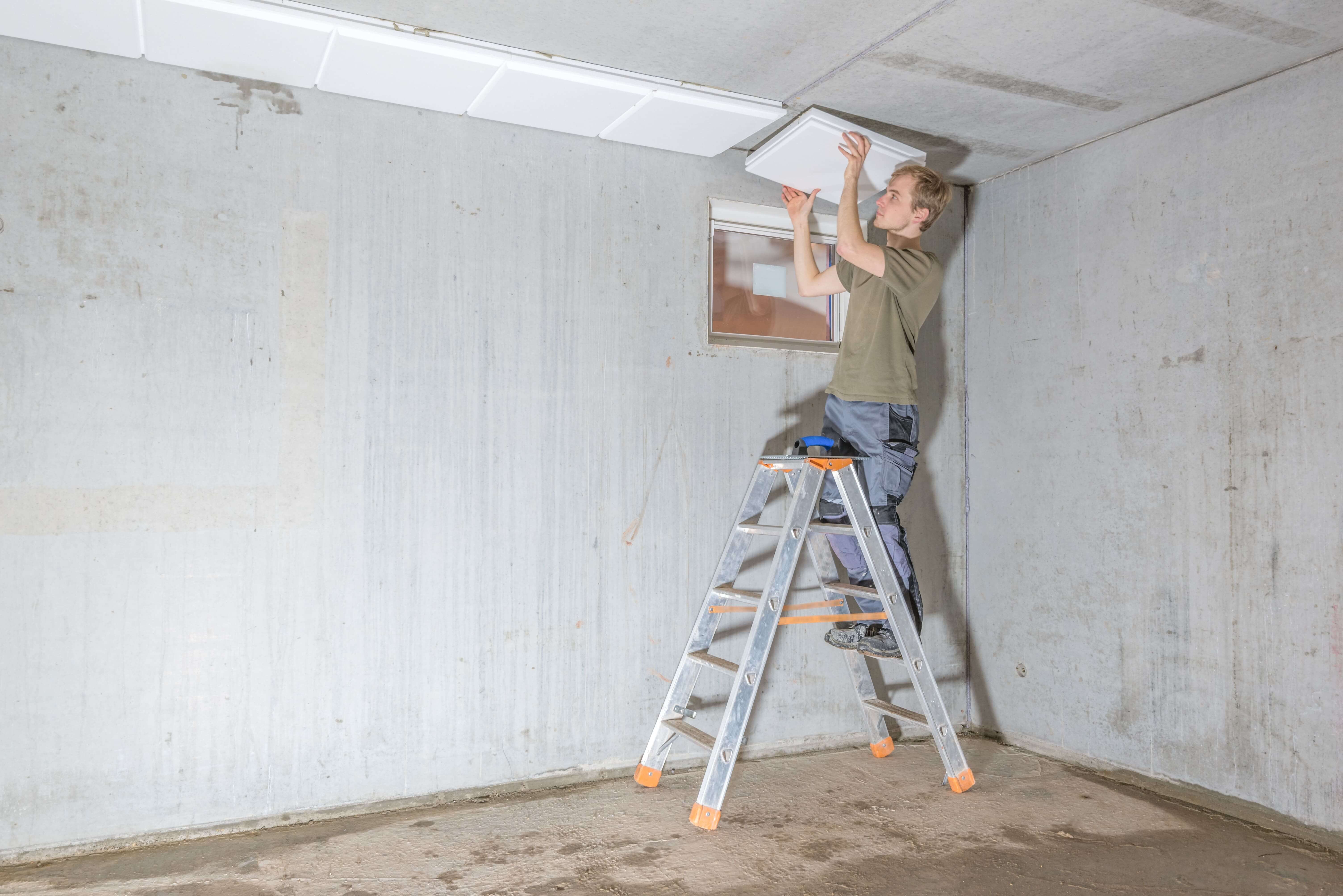Heimwerker dämmt auf einer Leiter stehend seine Kellerdecke