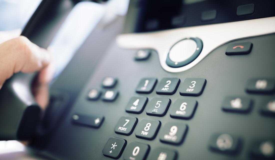 Bild mit Händen, die sich über einem Festnetztelefon bewegen.