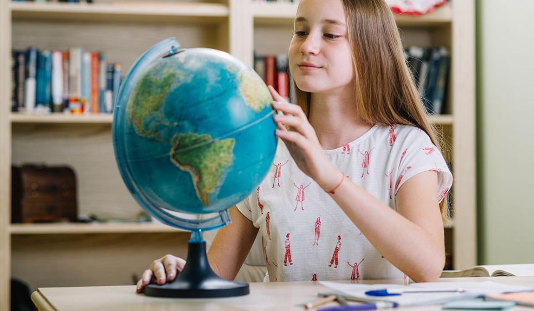 Eine Jugendliche betrachtet die Länder auf einem Globus. 