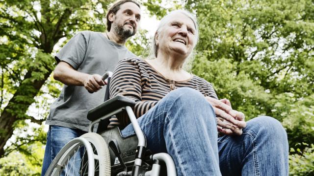 Eine ältere Frau sitzt im Rollstuhl und wird von einem jungen Mann angeschoben