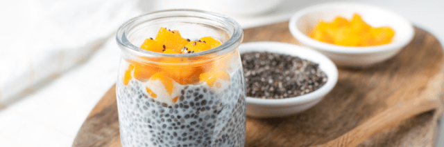 Auf einem Holzbrett steht ein Glas Joghurt, in den Chia-Samen gemischt sind.