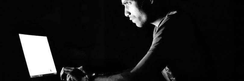 Düstere Schwarz-Weiß-Aufnahme eines Mannes, der vor einem Laptop sitzt