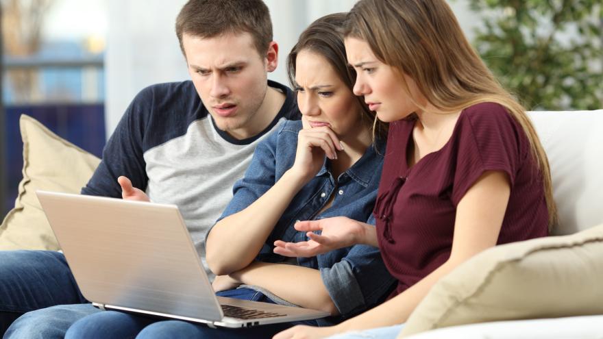 Drei junge Menschen sitzen auf der Couch und gucken verärgert auf einen Laptop.