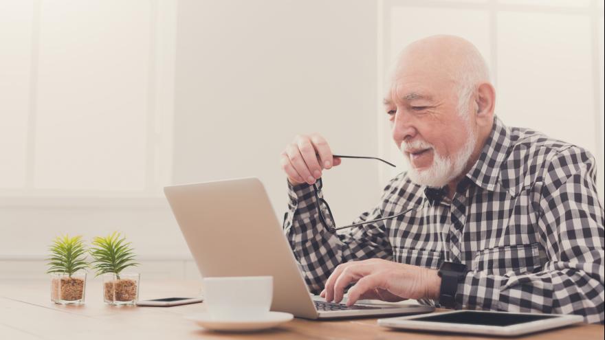 Älterer Mann sitzt am Schreibtisch mit Laptop
