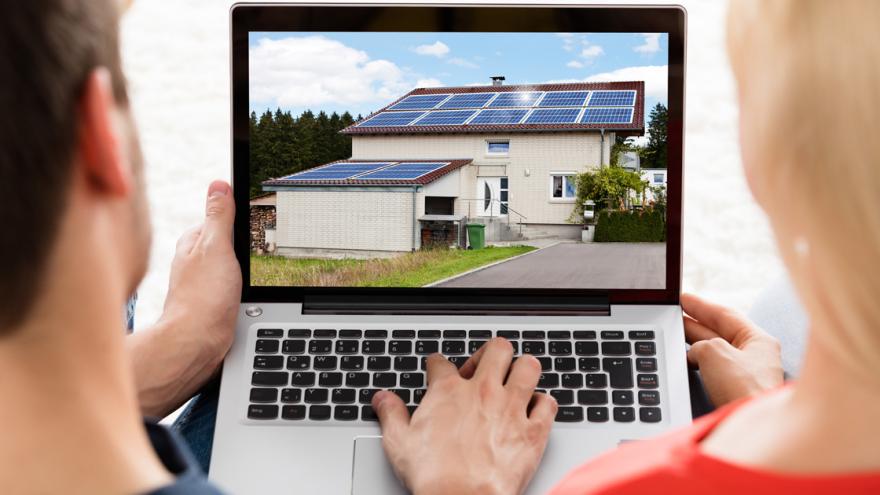 Ein Mann und eine Frau vor einem Laptop mit Foto eines Hauses mit Solardach