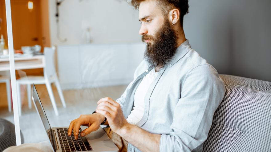 Junger Mann sitzt mit Laptop auf dem Sofa