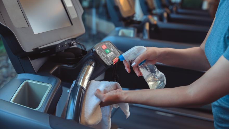 Mitarbeiterin eines Fitnessstudios desinfiziert ein Laufband