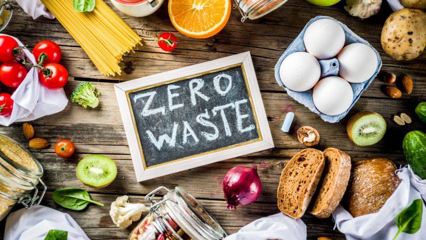Ein Schildchen mit der Aufschrift "Zero Waste" liegt zwischen Lebensmittel auf einem Tisch.
