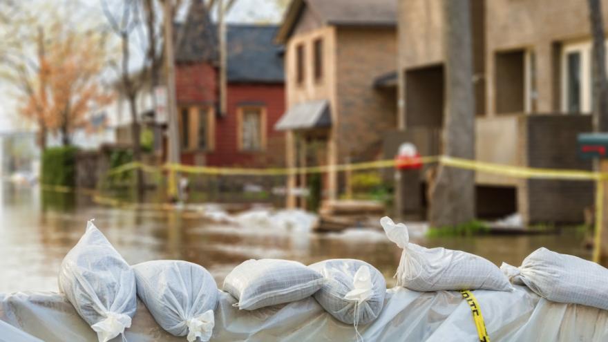 Eine Siedlung steht unter Wasser, auf der Straße sind Sandsäcke gestapelt.