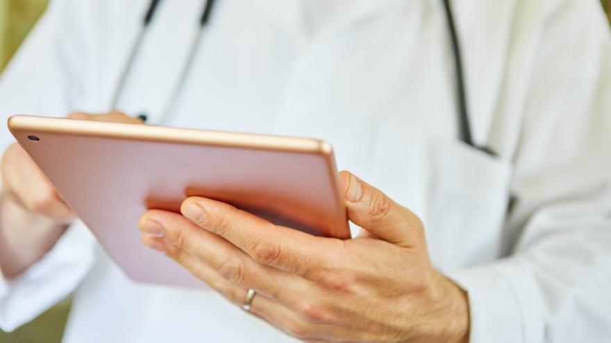 Arzt hält ein Tablett in der Hand, Bildausschnitt mit Hand, Tablett und Stethoskop