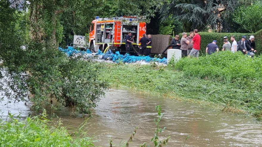 Feuerwehrwagen und Helfer an einem Fluss mit Sandsäcken