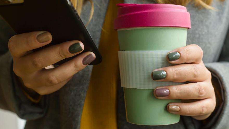 Junge Frau hält wiederverwertbaren Kaffeebecher in einer Hand