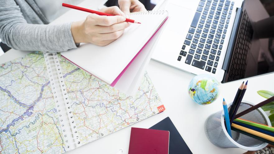 Frau bei der Reiseplanung_Bildausschnitt mit Karte, Laptop und Notizbuch