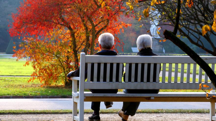 Zwei Senioren sitzen im herbstlichen Park auf einer Bank