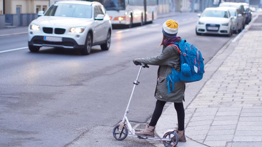 Kind überquert auf dem Schulweg mit einem Roller die Straße