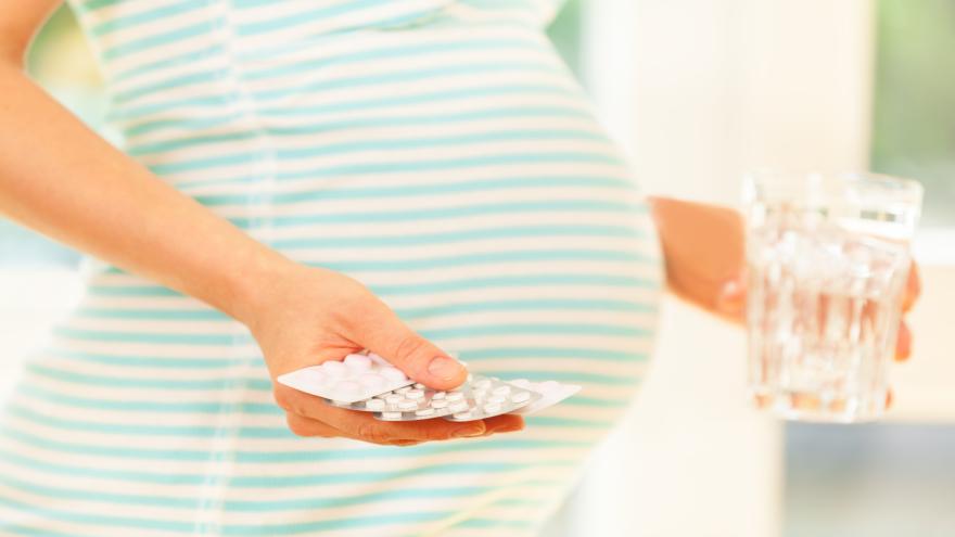 Schwangere Frau trägt Tabletten und Glas Wasser