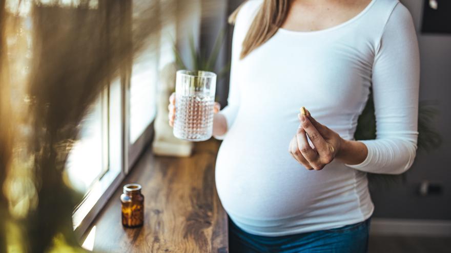 Schwangere hält eine Tablette und ein Glas Wasser in der Hand
