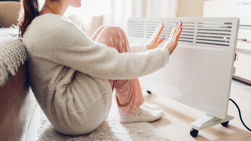Frau sitzt auf Boden vor Elektroheizung und wärmt sich die Hände