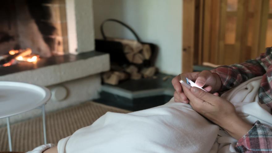Person sitzt vor Kamin auf Sofa und hat Handy in der Hand