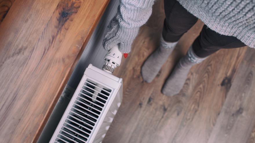 Frau mit Handschuh dreht an Thermostat der Heizung