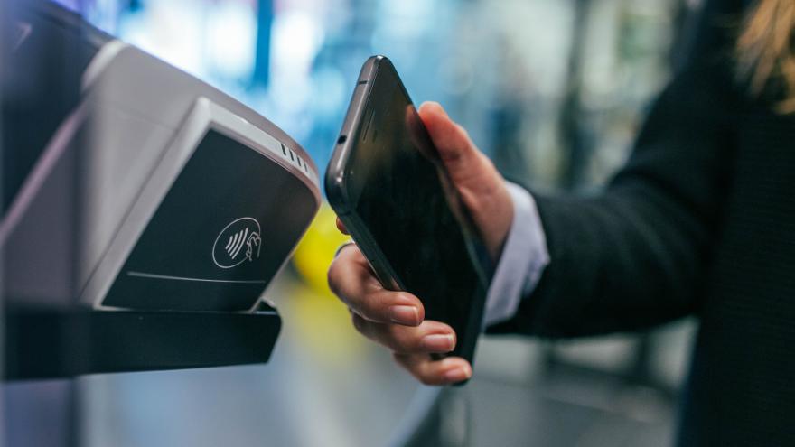 Ein Kunde hält sei Smartphone zum Bezahlen an Gerät zum kontaktlosen Bezahlen