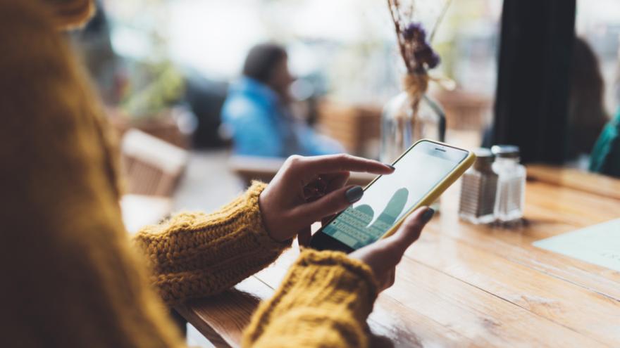 Eine Frau sitzt an einem Tisch und blickt auf ihr Smartphone.