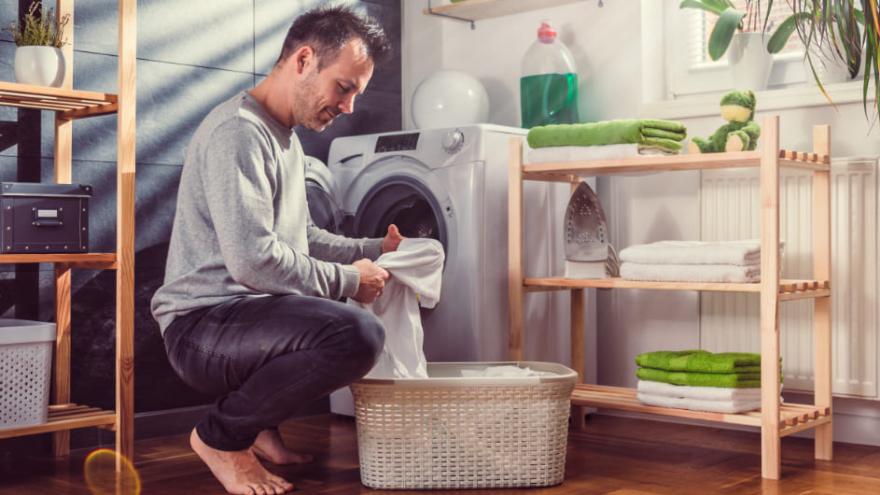 Mann kniet mit Wäsche vor Waschmaschine