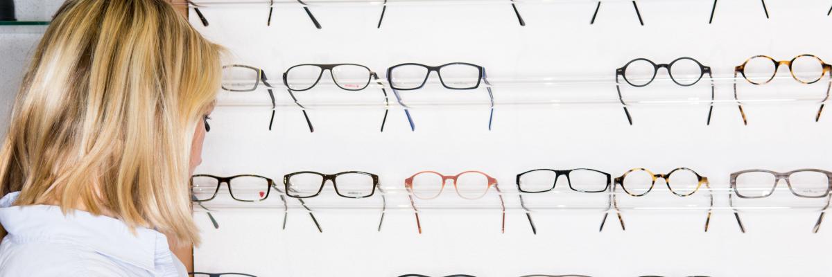 Eine Frau steht beim Optiker vor einer großen Auswahl an Brillen.