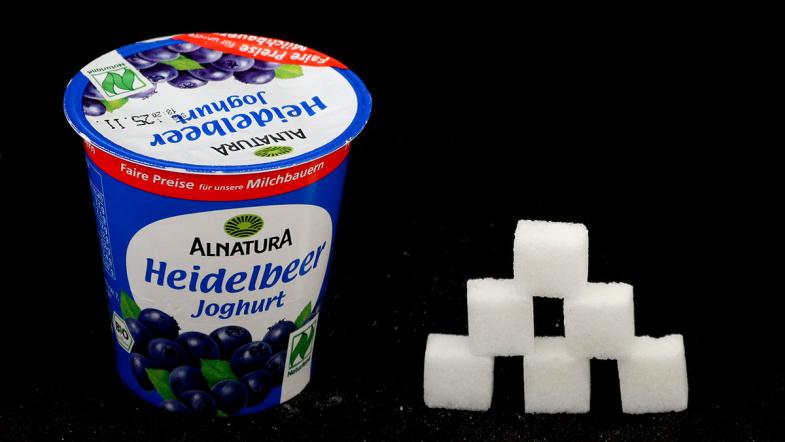 Joghurtbecher von Alnatura und daneben eine Zuckerwürfel-Pyramide