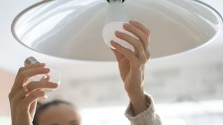 Frau tauscht Glühbirne durch Energiesparlampe aus