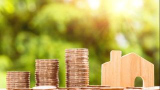 gestapelte Münzen neben einem kleinen Holzhaus