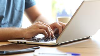 Mann schreibt auf Laptop, nur Hände sind sichtbar