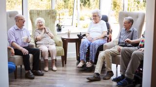 Mehrere Senioren sitzen in einem großen, hellen Raum zusammen.