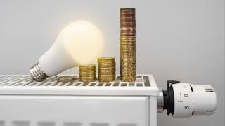 Brennende Glühbirne liegt mit einem Stapel Geldmünzen auf einer Heizung