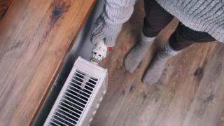 Frau mit Handschuh dreht an Thermostat der Heizung