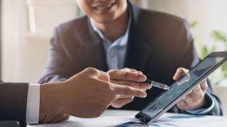 Mann in Anzug zeigt anderem Mann im Anzug etwas auf dem Tablett