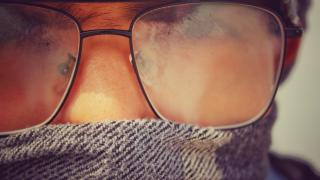 Ein Mann mit Schal um den Mund trägt eine Brille mit beschlagenen Gläsern