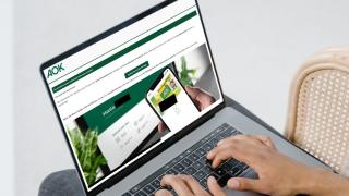 Zwei Hände auf der Tastatur eines aufgeklappten Laptops, auf dem Display eine Phishing-Mail mit AOK-Bezug