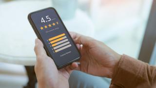 Jemand hält ein Handy in der Hand, auf dem eine Fünf-Sterne-Online-Bewertung zu sehen ist.