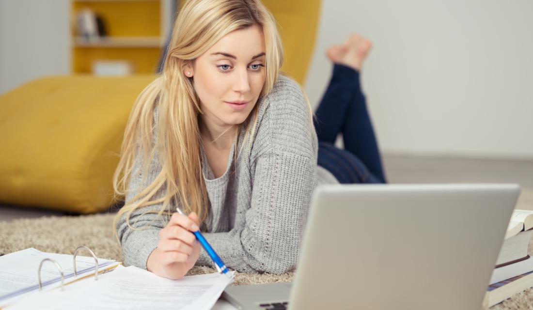 Junge Frau schaut auf Laptop und macht Notizen